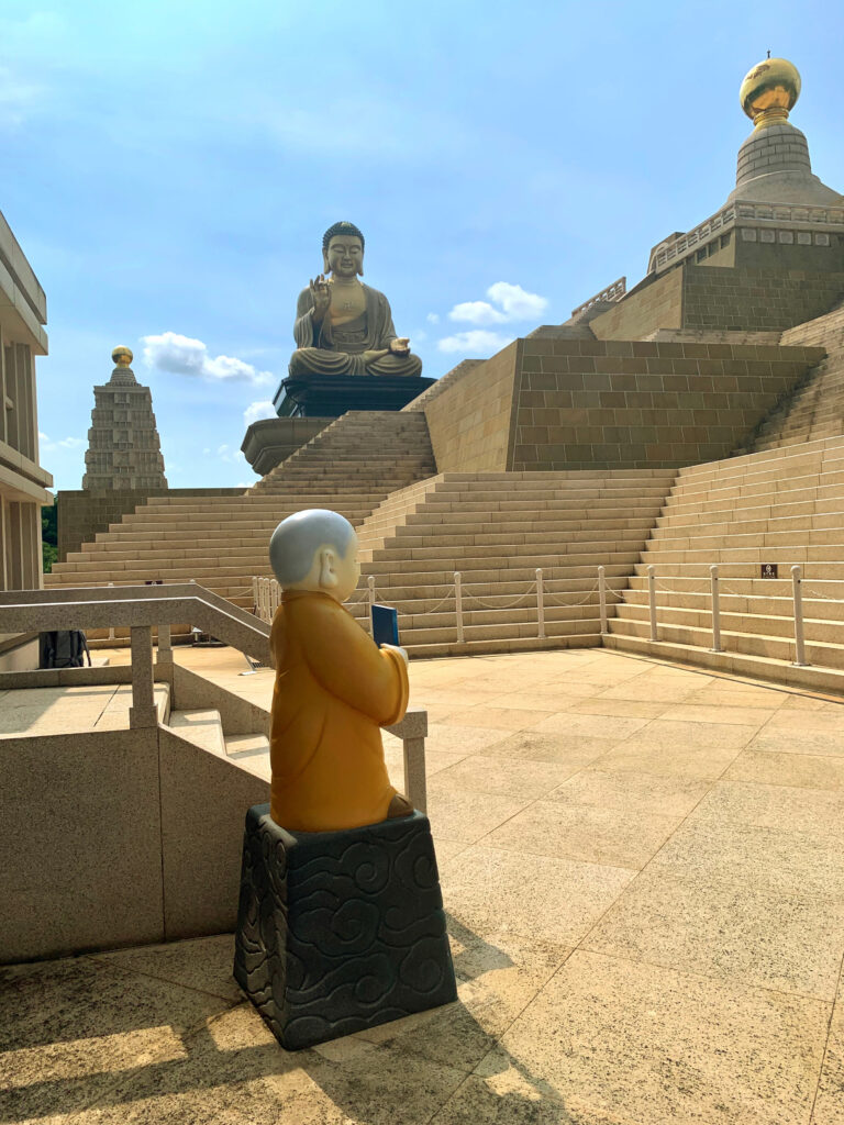 Fo Guang Shan -Der kleine Mönch vor einer Stupa und der große Buddha im Hintergrund